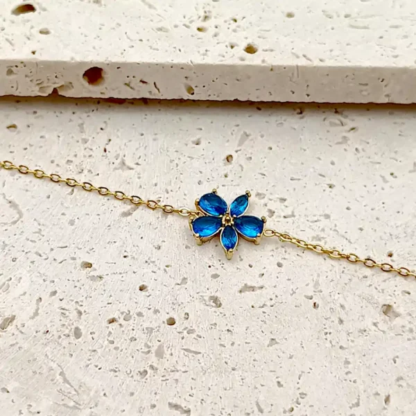 Bracelet doré en acier avec pendentif fleur en verre bleu.