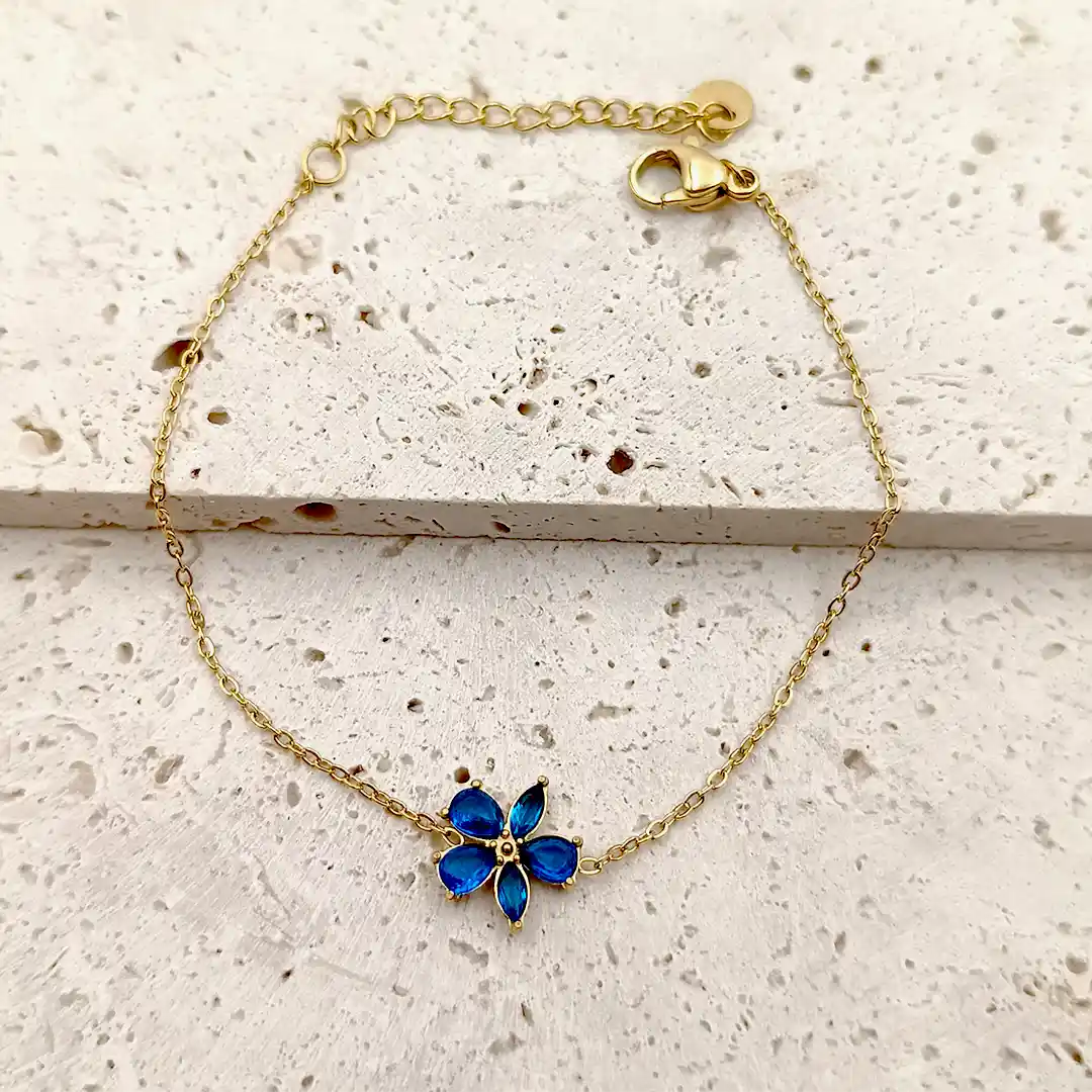 Bracelet doré en acier avec pendentif fleur en verre bleu.