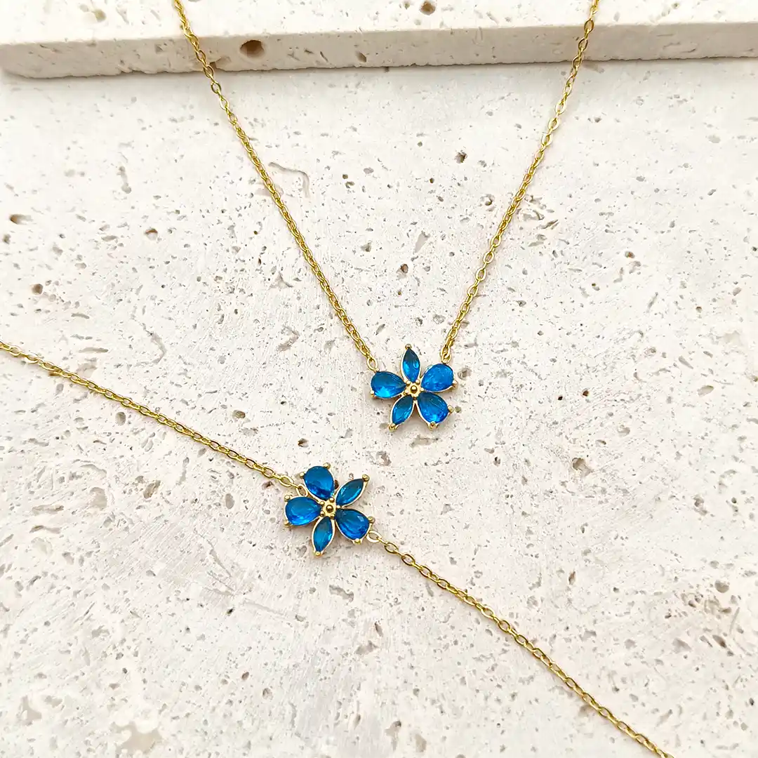 Colliers et bracelets assortis dorés en acier avec pendentif fleur en verre bleu.