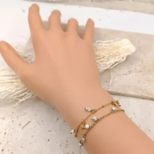 Bracelet fin en acier doré orné de perles blanches pendantes.