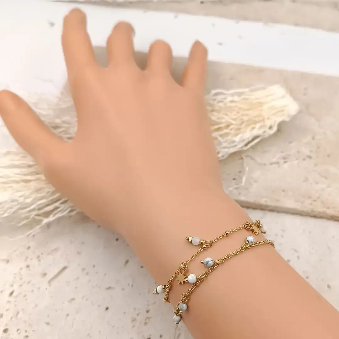 Bracelet fin en acier doré orné de perles blanches pendantes.