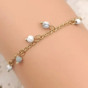 Bracelet fin en acier doré orné de perles blanches pendantes.