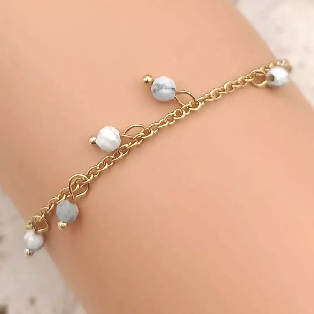 Bracelet fin en acier doré orné de perles blanches pendantes.