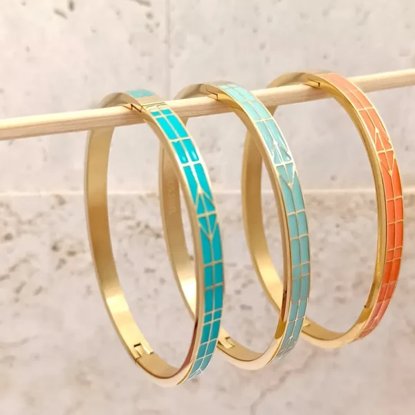 Ensemble de trois bracelets joncs en acier doré, décorés d’émaux colorés cyan, turquoise et orange avec motifs de flèches stylisées