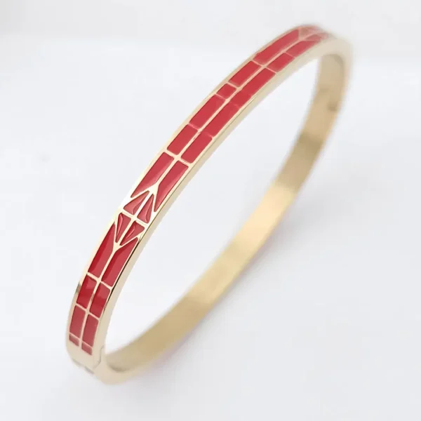 Bracelet jonc doré avec émaux rouges et motif flèche stylisée.