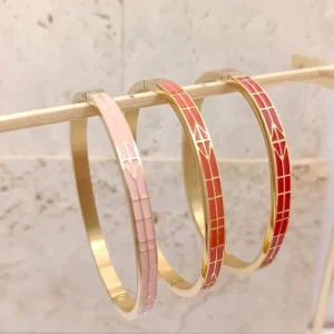Ensemble de trois bracelets joncs en acier doré, décorés d’émaux colorés rose, corail et rouge avec motifs de flèches stylisées