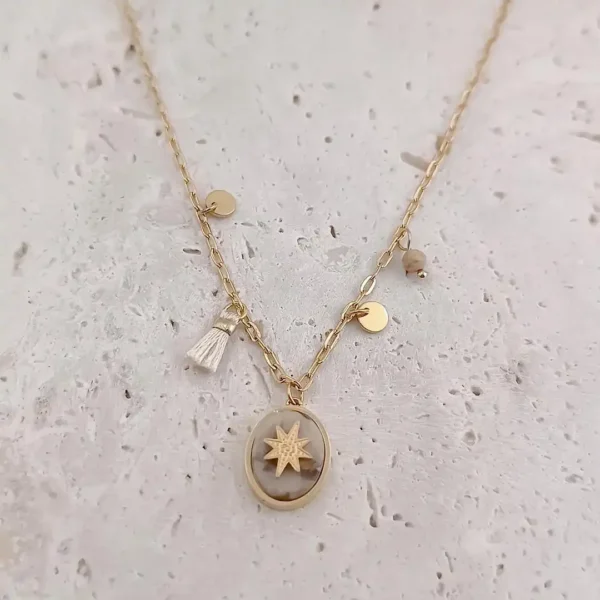 Collier en acier doré avec médaille ovale pierre jaspe étoile et breloques dorées et un pompon écru.