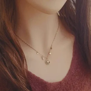 Collier en acier doré avec médaille ovale étoile et breloques dorées et blanches.