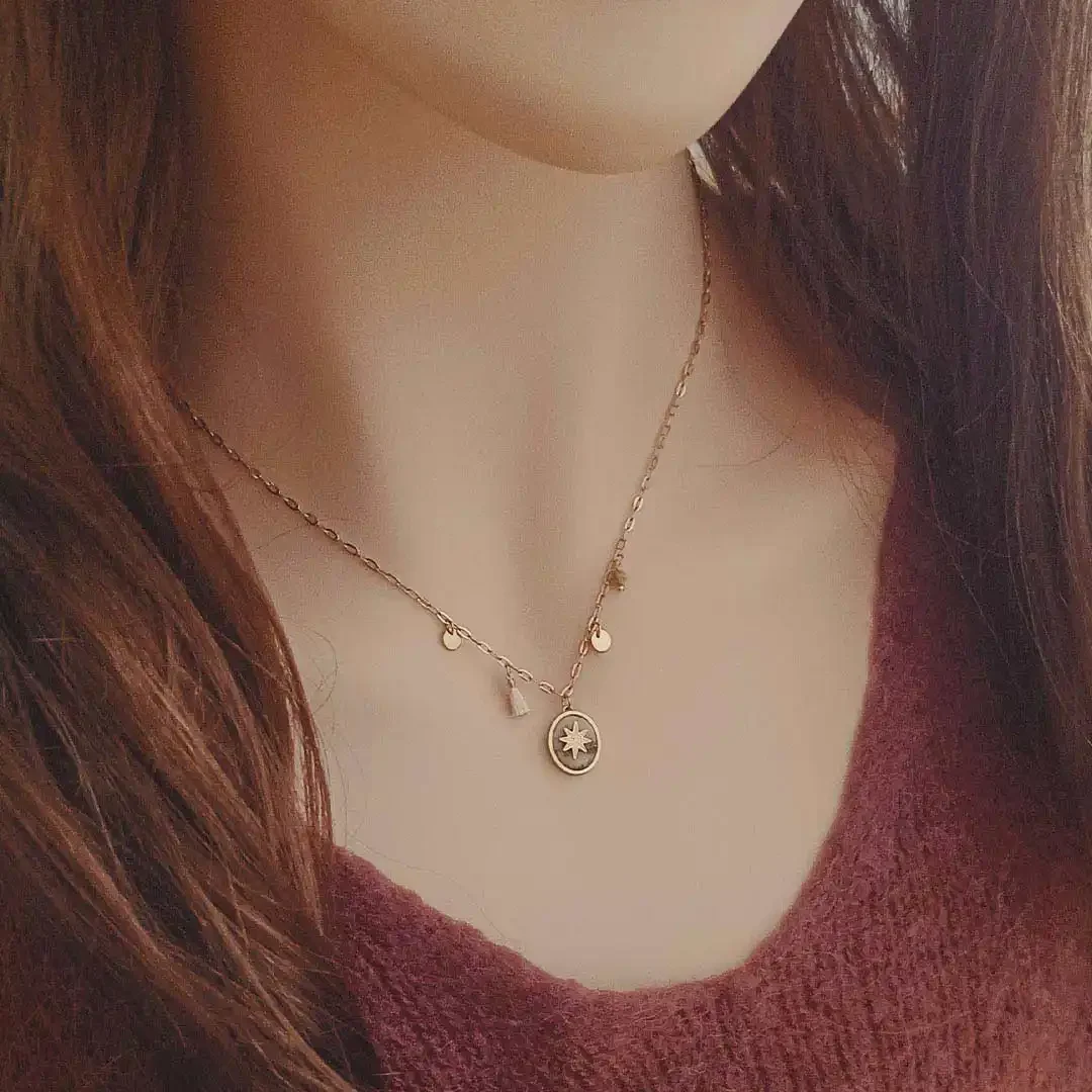Collier en acier doré avec médaille ovale étoile et breloques dorées et blanches.