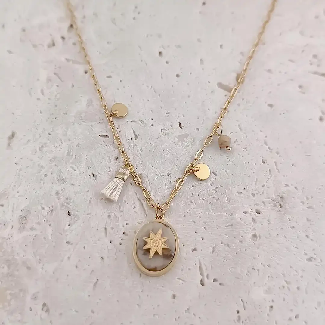 Collier en acier doré avec médaille ovale pierre jaspe étoile et breloques dorées et un pompon écru.