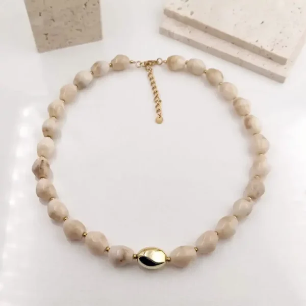 Collier acier en perles beiges irrégulières avec fermoir doré et perle centrale ovale dorée, bijou raffiné en résine.