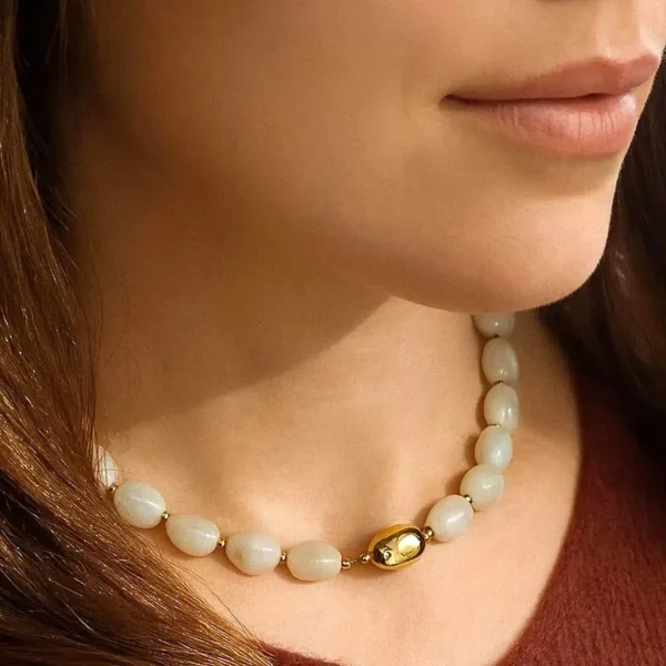 Collier acier en perles beiges irrégulières avec fermoir doré et perle centrale ovale dorée, bijou raffiné en résine.