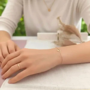 Bracelet fin en acier doré avec pendentif cœur ajouré et petit cœur pailleté au centre.