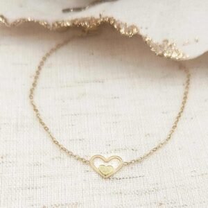 Bracelet fin en acier doré avec pendentif cœur ajouré et petit cœur pailleté au centre.