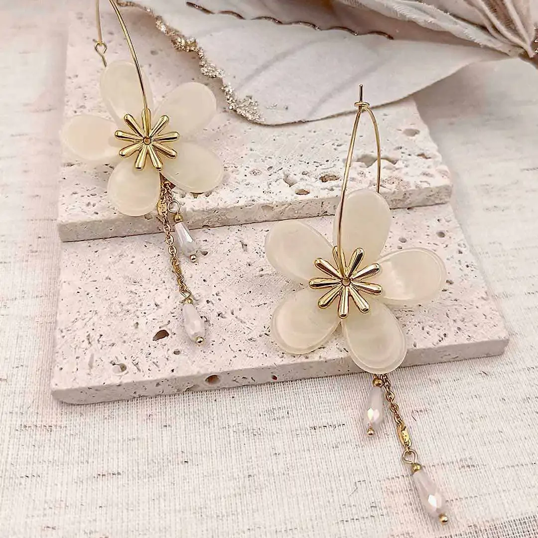 Boucles d’oreilles créoles dorées avec fleurs en résine couleur créme et pampilles délicates, bijou élégant et féminin.