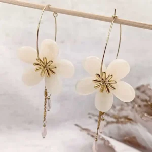 Boucles d’oreilles créoles dorées avec fleurs en résine couleur créme et pampilles délicates, bijou élégant et féminin.