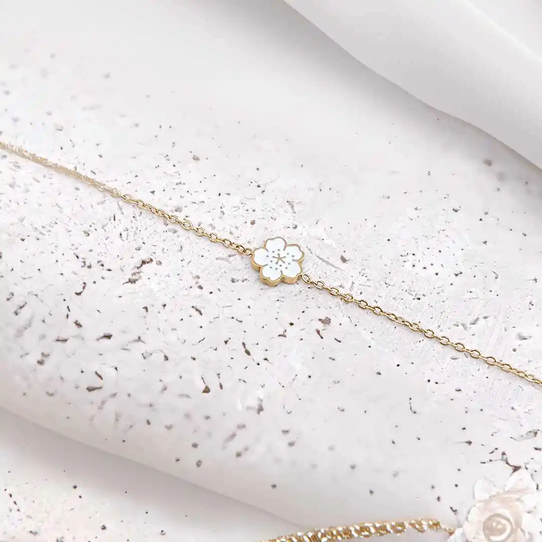 Bracelet enfant en acier inoxydable doré avec fleur émaillée de couleur blanche.
