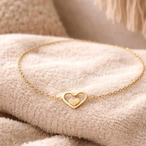 Bracelet fin en acier doré avec pendentif cœur ajouré et petit cœur pailleté au centre.