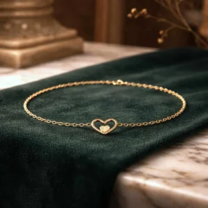 Bracelet fin en acier doré avec pendentif cœur ajouré et petit cœur pailleté au centre.