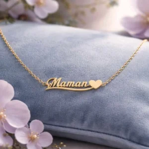 Collier doré en acier inoxydable avec inscription “Maman” et petit cœur, posé sur coussin bleu, idée cadeau Fête des Mères élégante et durable.