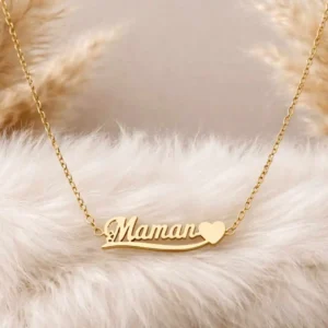 Collier doré en acier inoxydable avec inscription “Maman” et petit cœur, posé sur coussin bleu, idée cadeau Fête des Mères élégante et durable.