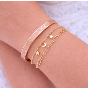 Bracelet jonc rose et bracelets fins dorés portés en accumulation sur le poignet d’une femme, bijou tendance