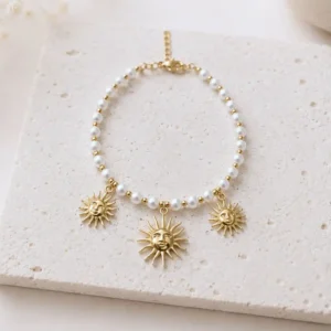 Bracelet soleil en acier doré avec perles blanches et trois breloques soleil