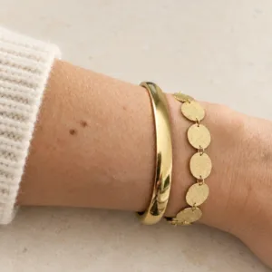 Bracelet femme doré à pastilles rondes texturées associé à un bracelet jonc doré lisse sur le même poignet.