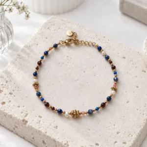 Bracelet petites pierres bleues et perles dorées en acier inoxydable, avec perles brunes et blanches, fermoir mousqueton et chaînette d'extension.