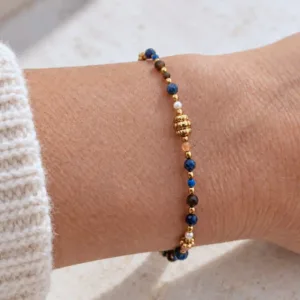 Bracelet femme à petites pierres bleues et brunes, perles blanches et détails dorés, avec perle centrale travaillée, au poignet.