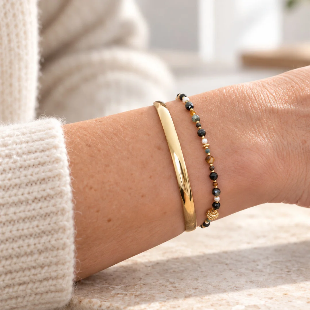 Bracelet femme à petites pierres foncées et perles multicolores, associé à un jonc doré lisse au poignet.