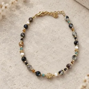 Bracelet petites pierres noires et grises en acier inoxydable doré, avec perles colorées, détail central travaillé et fermoir mousqueton.