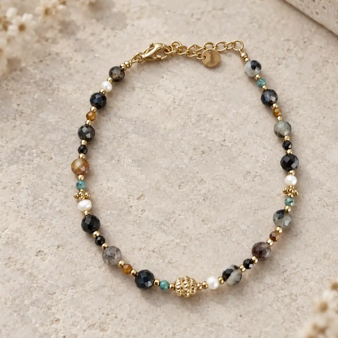 Bracelet petites pierres noires et grises en acier inoxydable doré, avec perles colorées, détail central travaillé et fermoir mousqueton.