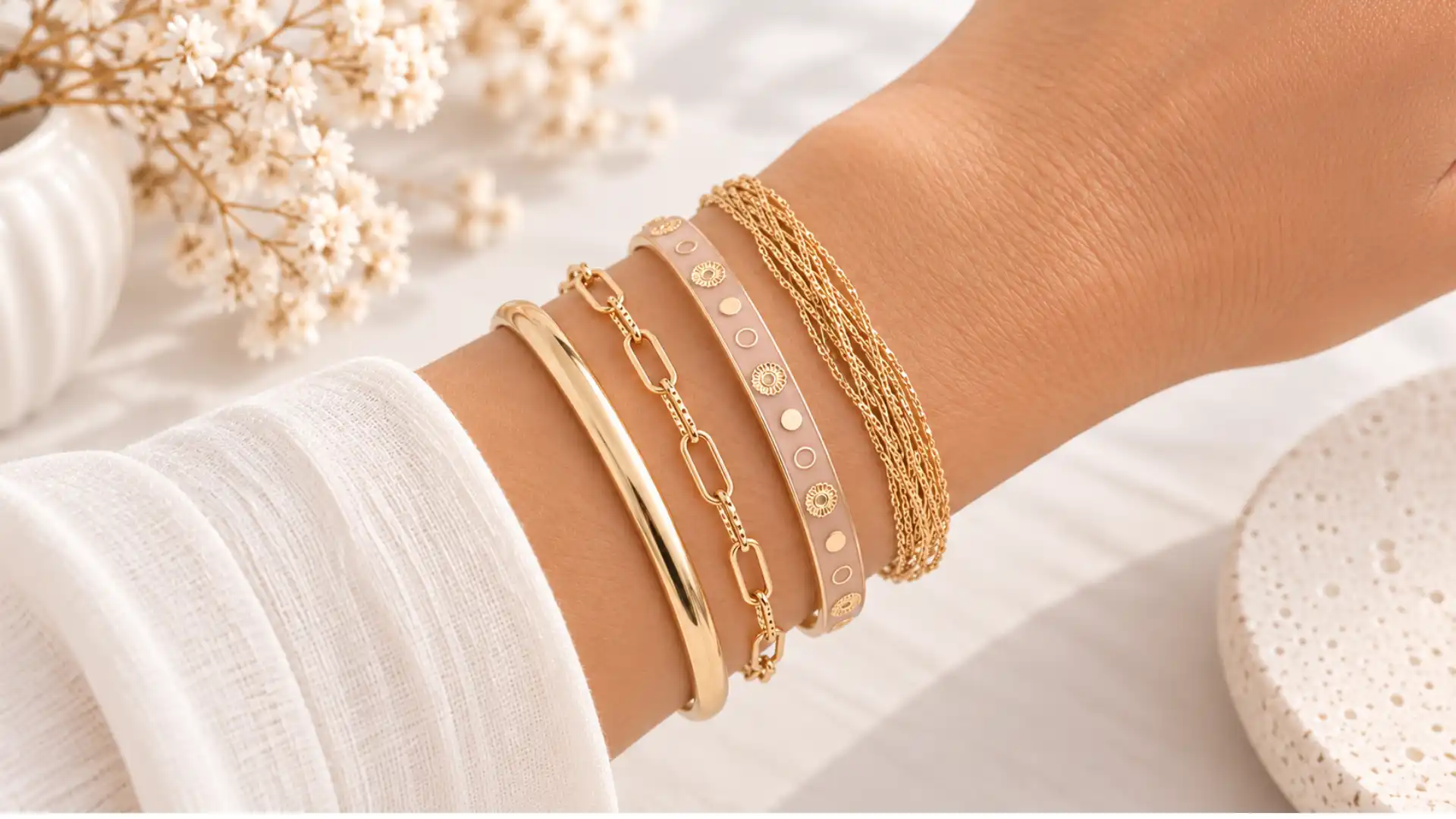 Bracelets femme tendance 2026-2027 en accumulation avec chaînes dorées, jonc émaillé rose et bracelet à maillons.